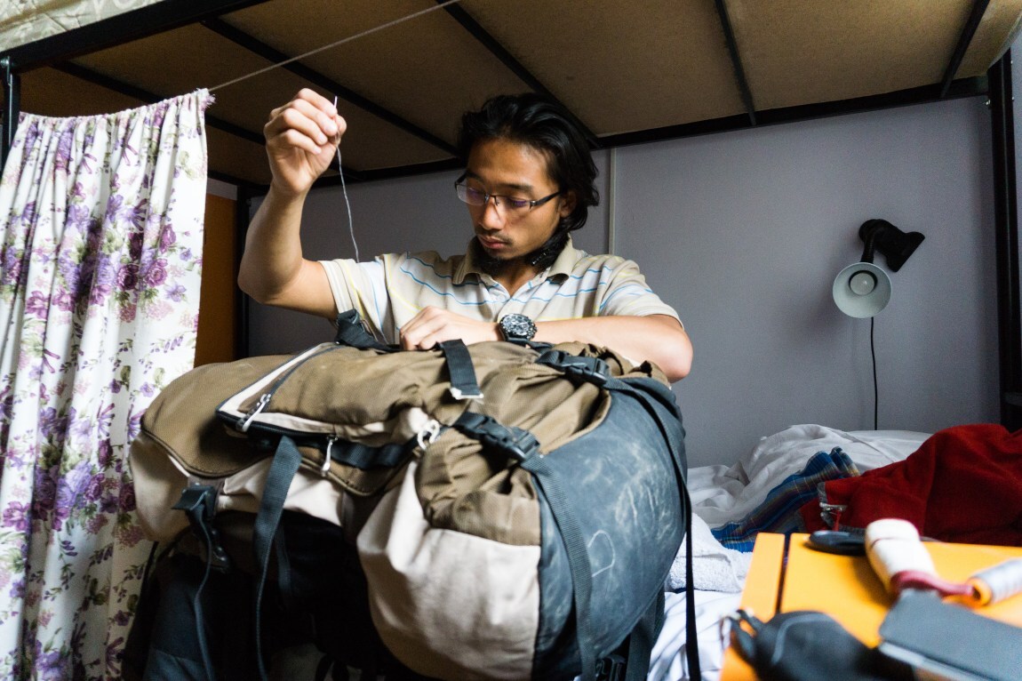 Mending backpack - Pure Odyssey a guy focusing on mending his tore backpack